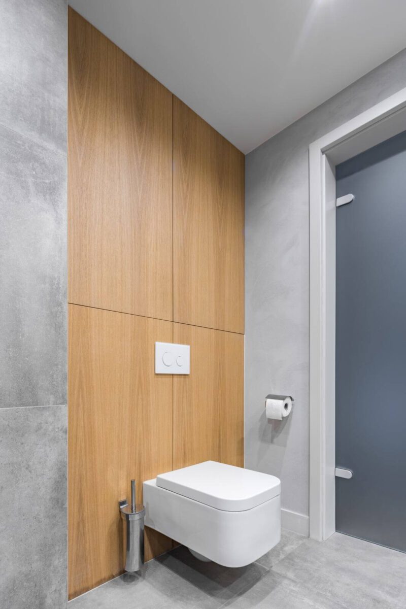 Gray bathroom with white toilet, and modern tiling with wooden details