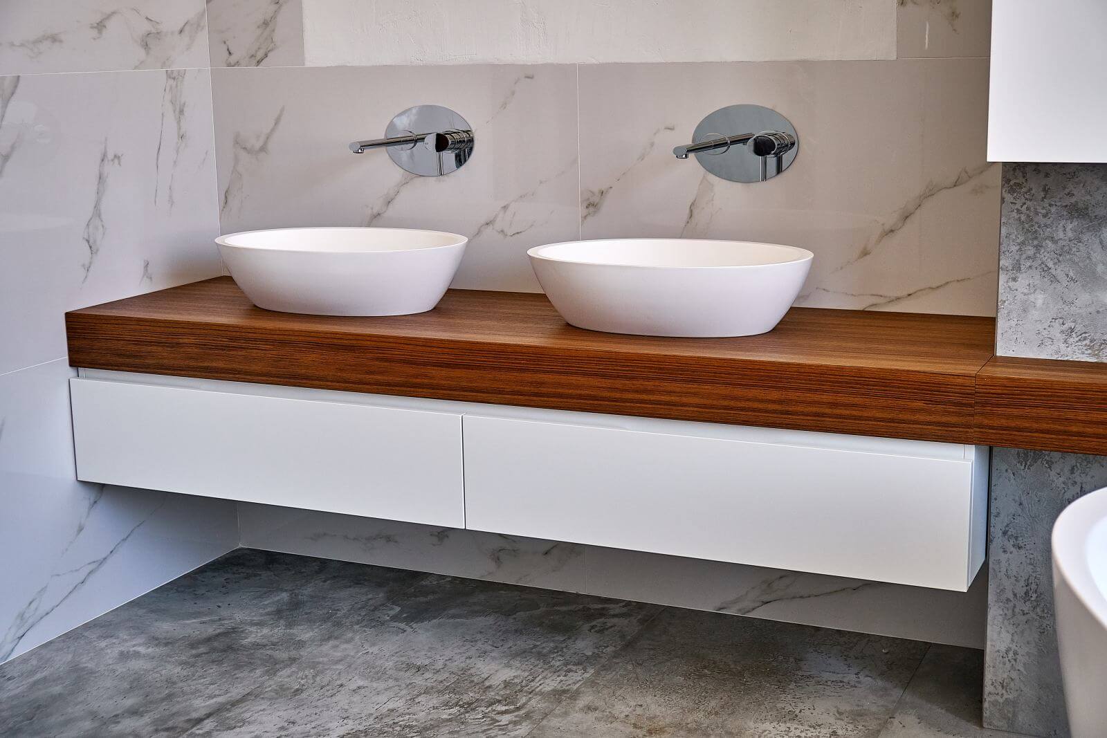 Ceramic round sinks placed on teak tabletop in luxury water closet with gray and white marble walls