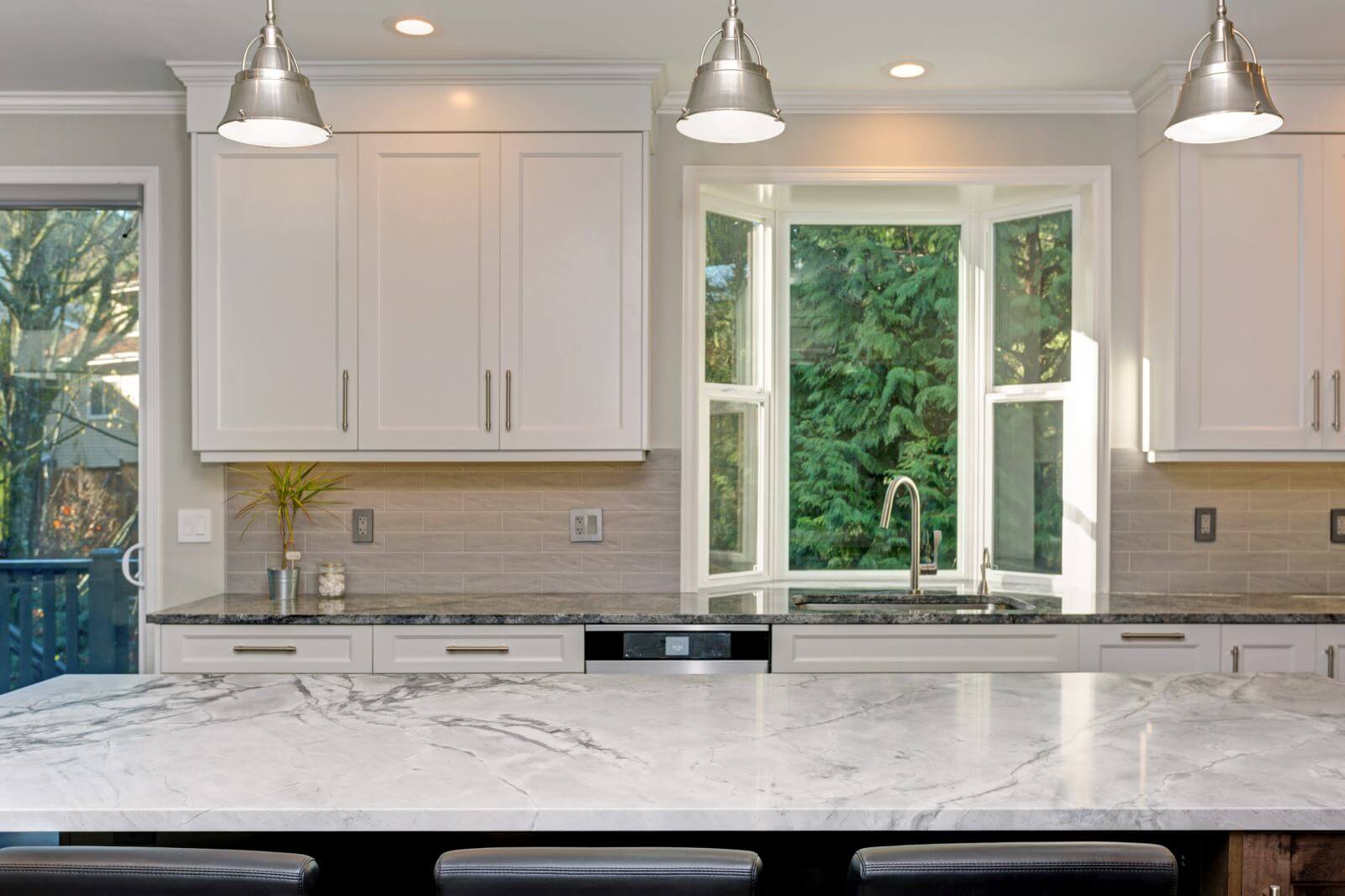 Luxury home interior boasts amazing white kitchen with custom white shaker cabinets, endless marble topped kitchen island and taupe tiled backsplash.