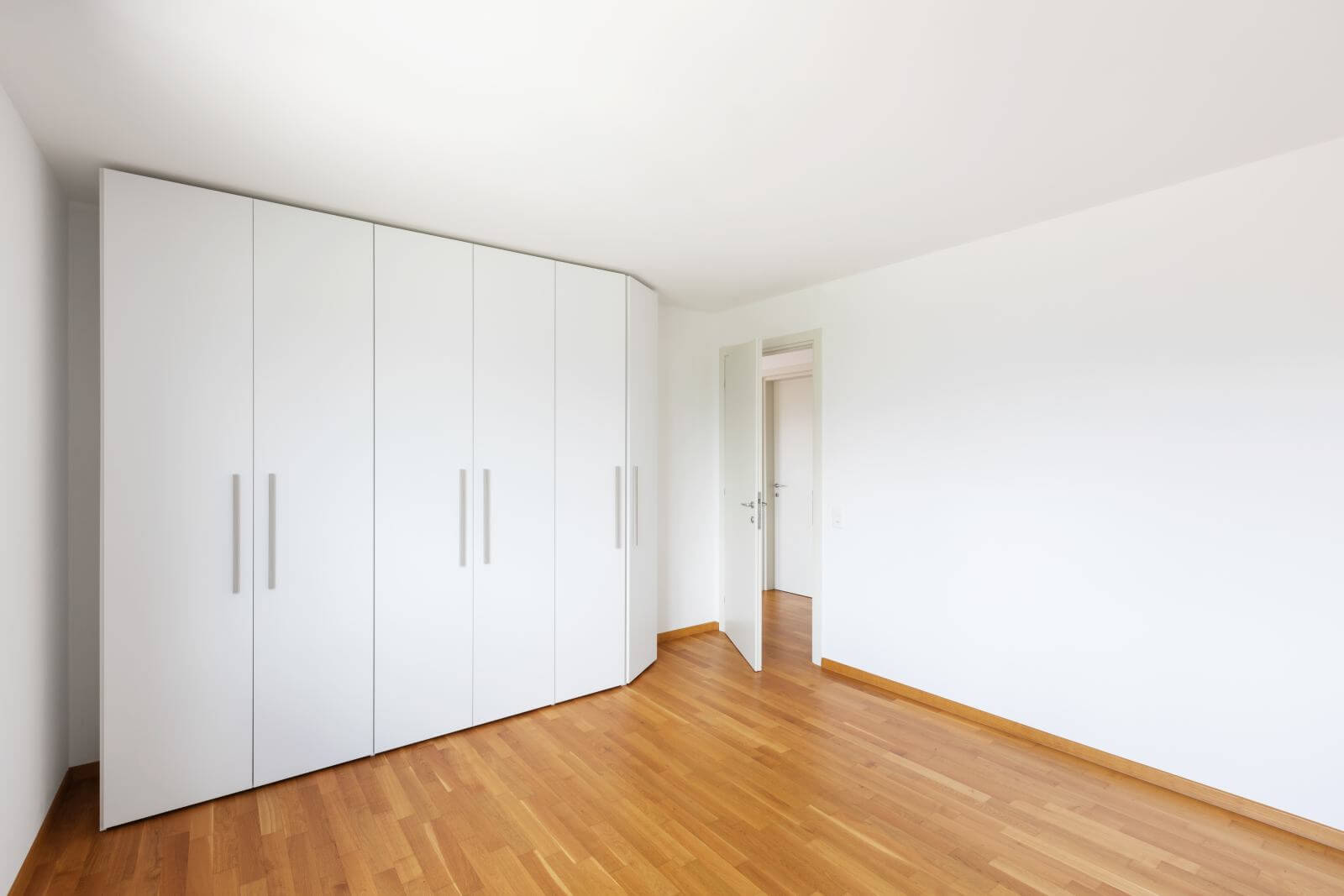 White empty room with large white wardrobe and open door on the corridor. Nobody inside