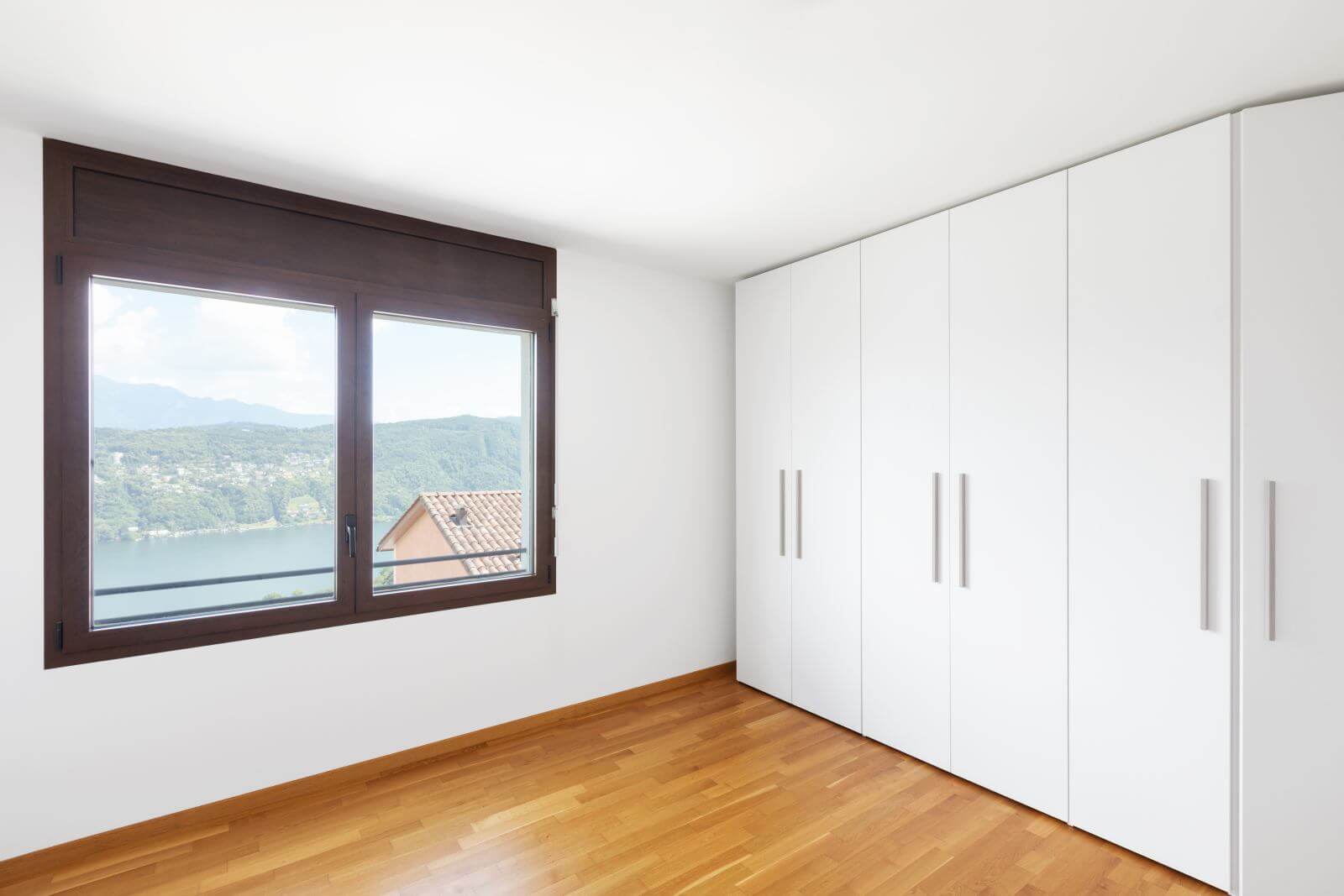 White empty room with windows overlooking the lake and large white wardrobe. Nobody inside