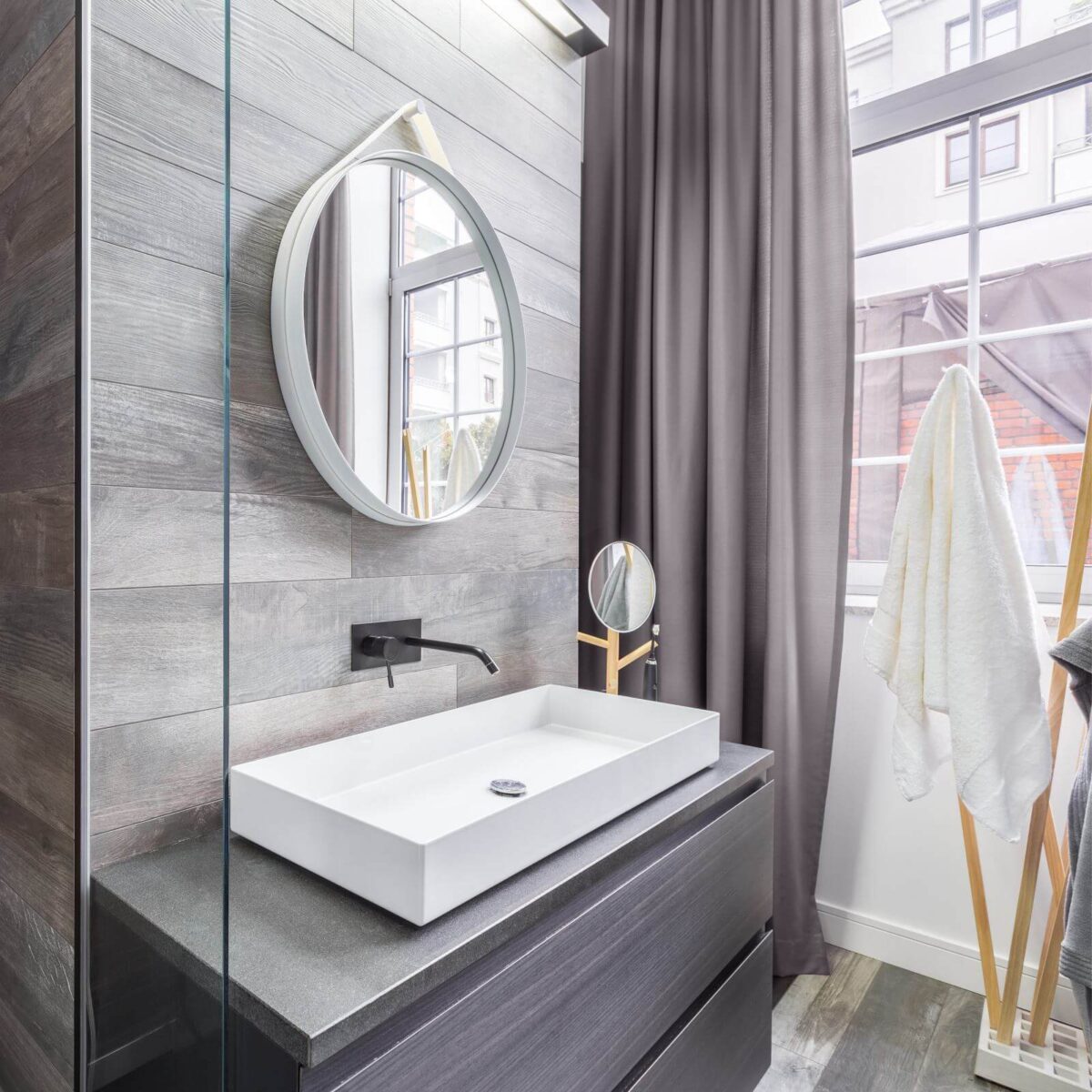Elegant design bathroom with wooden walls, white basin and round mirror